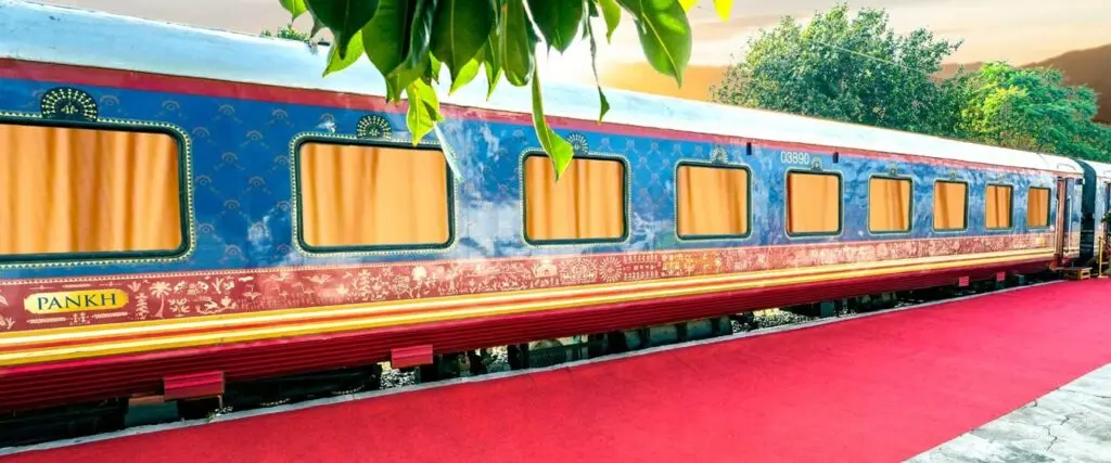 Hand-painted blue and maroon luxury rail carriage alongside a red carpet at sunset