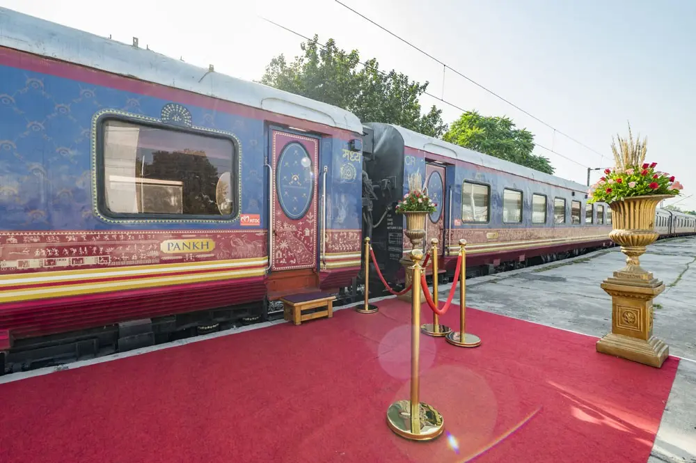 Royal-blue luxury train carriages beside a red carpet and gold stanchions on a station platform
