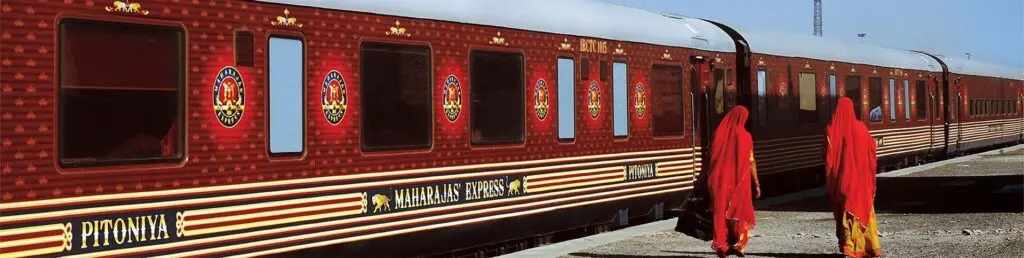 Maharajas' Express carriages at a sunny Rajasthan platform as two women in red saris walk past