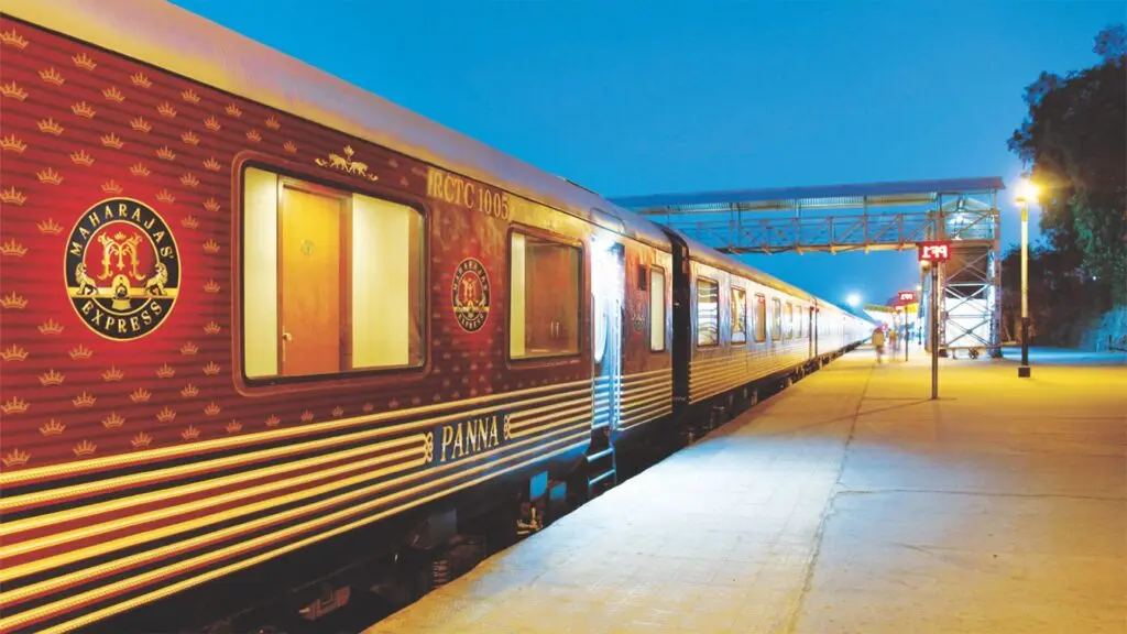 Maharajas' Express red and gold carriage waiting at a lit station platform at dusk