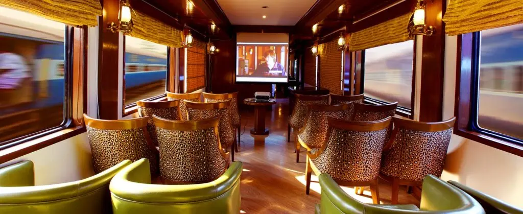 Safari lounge car with leopard-print armchairs facing a film screen, brass lanterns on the walls